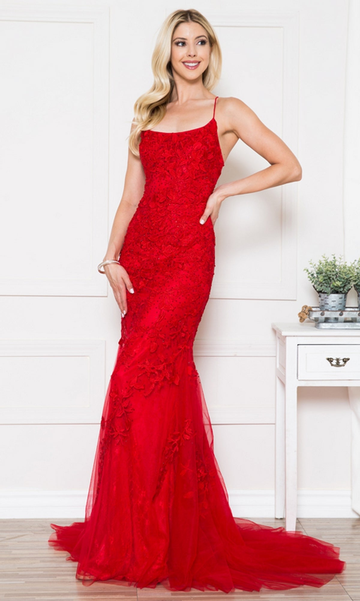 A woman poses indoors beside a white table with potted plants, wearing the Embroidered-Lace Tight Long Prom Gown 799—a sleeveless, floor-length gown with thin straps and elegant lace embroidery.